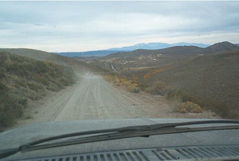 1986 Ford Bronco - Driving down a remote dirt road through a vast, arid landscape with distant mountains.