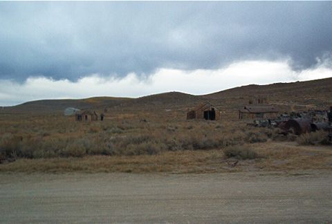 1986 Ford Bronco - A desolate scene unfolds with weathered structures scattered across a dry, brush-covered terrain beneath an overcast sky.
