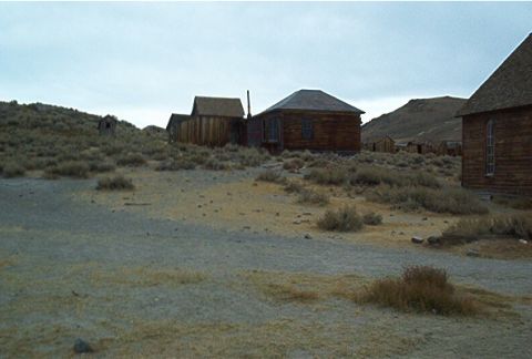 1986 Ford Bronco - Old wooden structures stand in a desolate, overgrown area, suggesting a ghost town.