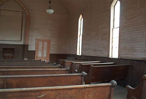1986 Ford Bronco - The interior of an old church shows rows of wooden pews and tall, arched windows, suggesting a historical or abandoned setting.