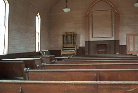 1986 Ford Bronco - The interior of an old church features rows of wooden pews facing a pipe organ and a large framed area on the wall.