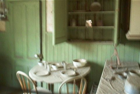 1986 Ford Bronco - An old, dusty interior scene shows a table with plates and bowls, and shelves with various items.
