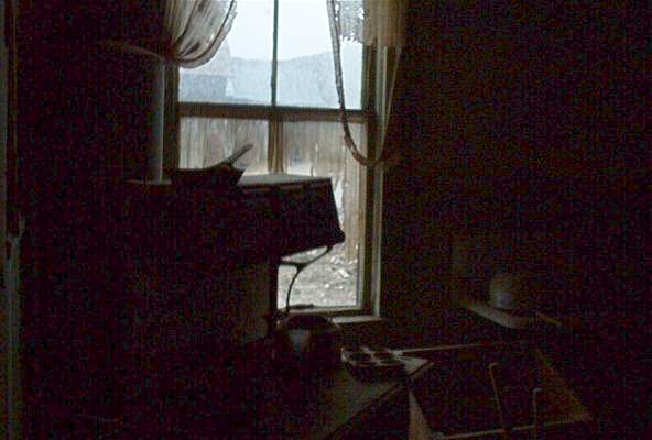 Dark room interior with a window showing an overcast sky and some distant structures