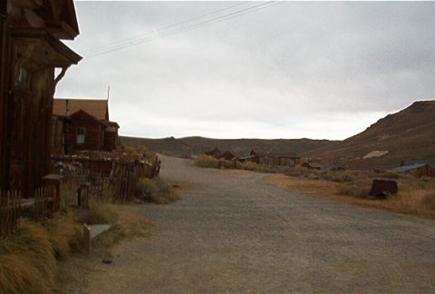 1986 Ford Bronco - A desolate ghost town scene with weathered wooden structures and a gravel road winding through the landscape.
