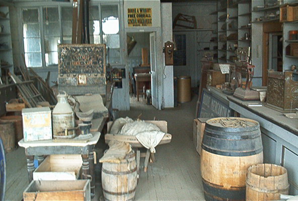 Interior of a dusty general store with barrels, scales, and shelves stocked with goods