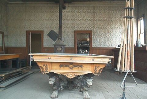 1986 Ford Bronco - An antique pool table with ornate carvings and lion-shaped legs sits in a room with a potbelly stove and pool cues.