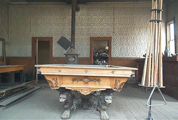 Old pool table with lion legs, wood paneling, and a potbelly stove