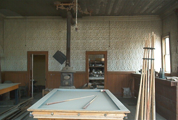 Interior of a dusty room with a pool table, pool cues, and a wood stove