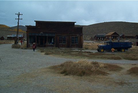 1986 Ford Bronco - A vintage blue truck sits idle in a deserted town, with a lone figure walking away from a general store.