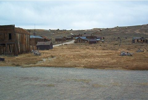 1986 Ford Bronco - A view of an abandoned town with weathered wooden structures and overgrown fields.