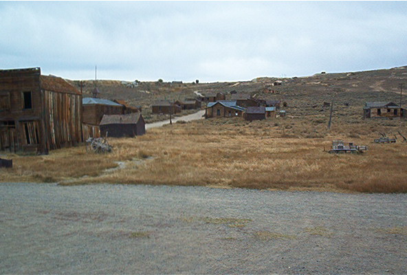 Ghost town with old buildings and dry grass under a cloudy sky