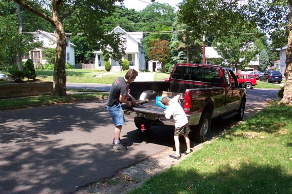 Red pickup truck with tailgate down, two people loading items into the bed