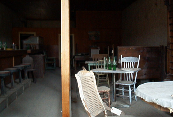 Interior of a room with a bar, stools, tables, chairs, and bottles
