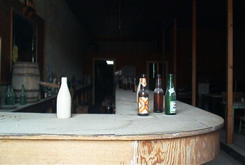 1986 Ford Bronco - The interior of a dusty bar scene, complete with bottles on the counter and a wooden barrel.