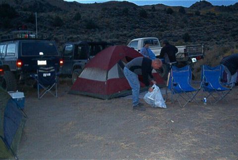 1986 Ford Bronco - Campers set up tents and chairs next to their off-road vehicles in a remote, hilly area.