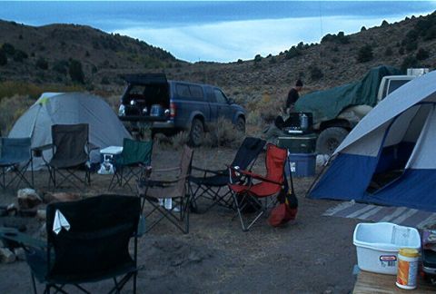 1986 Ford Bronco - A campsite is set up with tents, chairs, and two vehicles in a dry, hilly landscape.