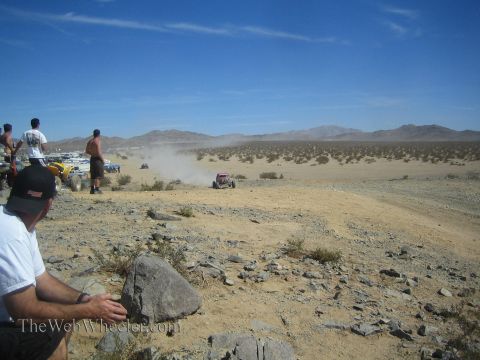 1990 Ford Bronco - Spectators sit on a rocky overlook watching off-road race vehicles raise dust across the distant desert valley.