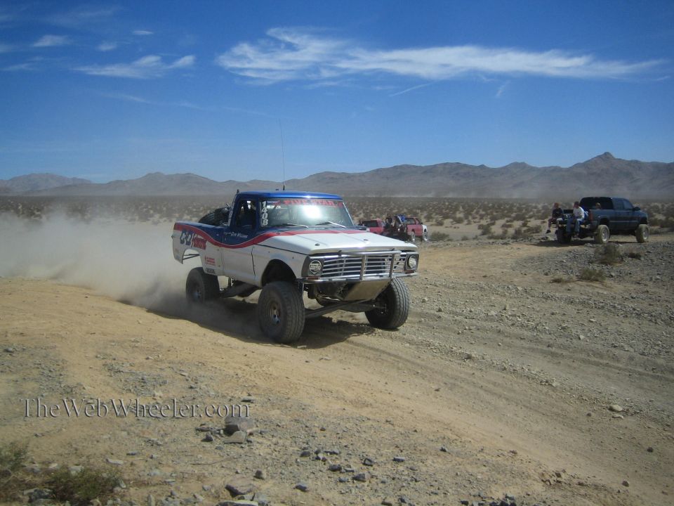 Vintage white and blue off-road race pickup on a desert trail with chase trucks