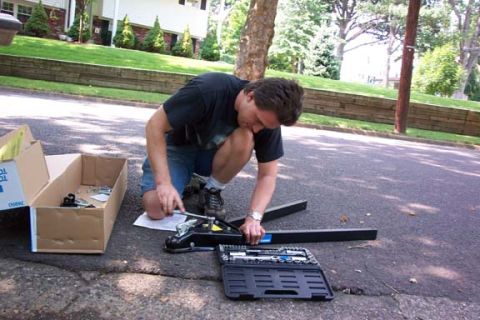 1979 Ford Bronco - Man works on a tow hitch assembly with a toolbox and parts laid out on the ground.