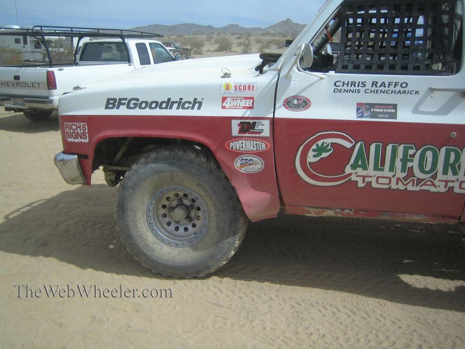Front quarter of a red and white off-road race truck with sponsor decals in desert