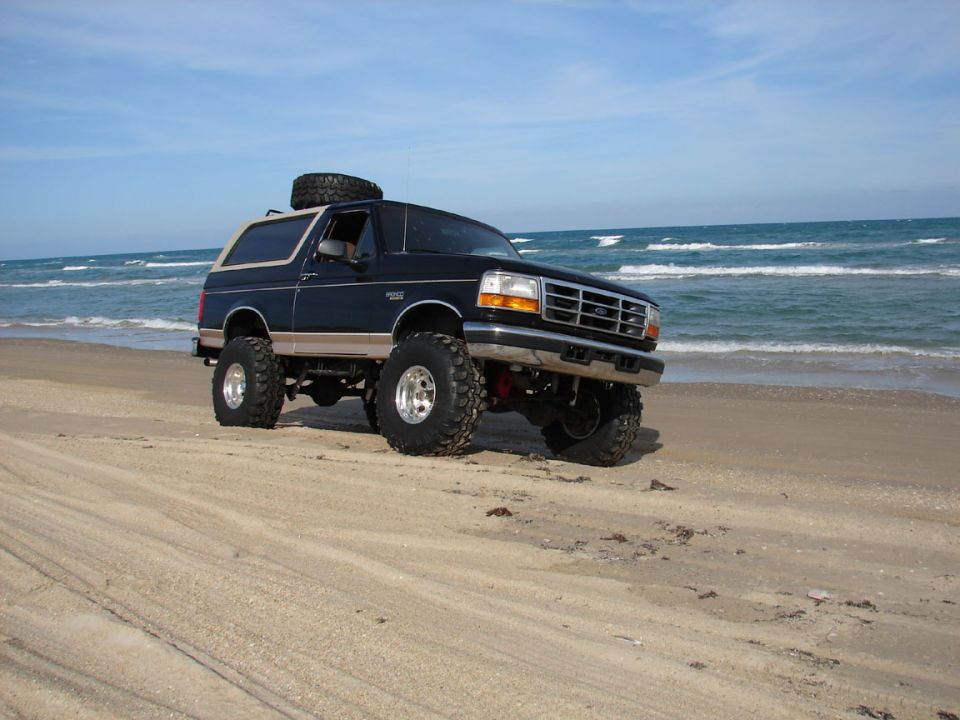 Lifted blue and tan Ford Bronco SUV parked on a beach by the ocean