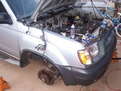 2005 Ford Mustang - The front wheel and engine bay of a silver Nissan Xterra are visible, with tools and a can of spray on the engine.