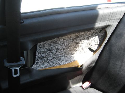1974 Ford F-100 - The interior door panel of a car shows damage and exposed insulation, with a seatbelt visible.