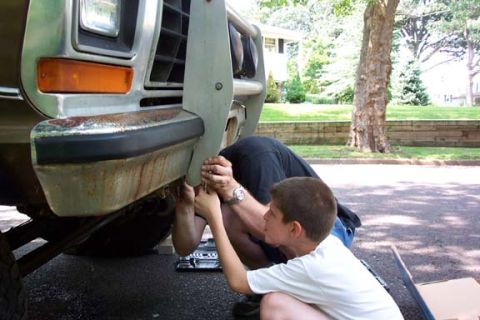 1979 Ford Bronco - A man and a boy are working on the front bumper of a vehicle, possibly a truck.