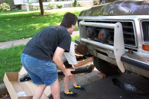 1979 Ford Bronco - Two individuals are working on the front bumper of a 1979 Ford Bronco, possibly installing a towbar.