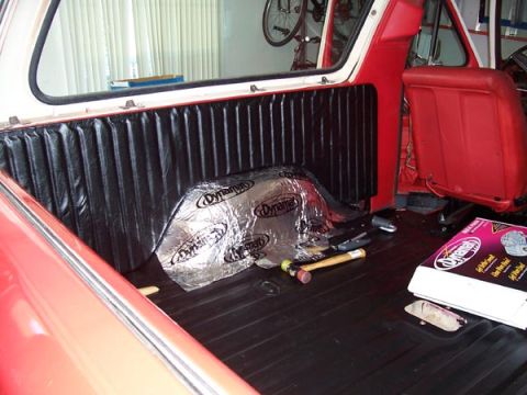 1978 Ford Bronco - The interior of a red vehicle shows sound deadening material on the wheel well and a red seat.