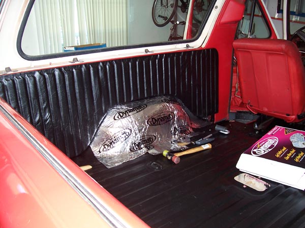 Red vehicle interior with black ribbed paneling, sound deadening material on wheel well, and a red seat