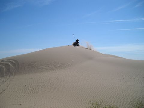 1993 Ford Bronco - An ATV navigates a sandy dune, creating a cloud of dust against the clear blue sky.