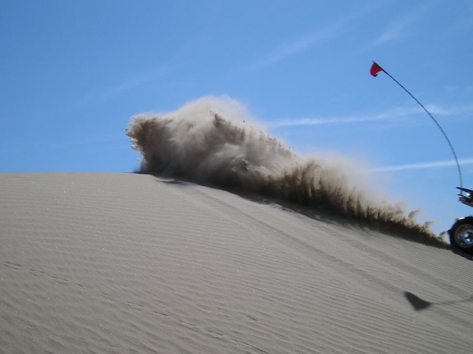 Off-road vehicle on a sand dune kicking up a large cloud of dust