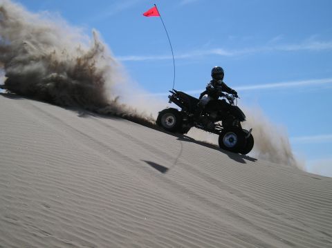 1993 Ford Bronco - An ATV rider navigates a sandy slope, creating a large dust cloud against a clear blue sky.