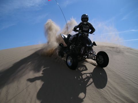 1993 Ford Bronco - Rider on a quad bike powers through sand on a dune under a blue sky.