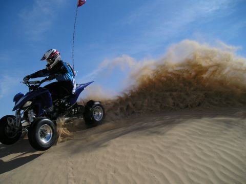 1993 Ford Bronco - A rider on a blue ATV navigates a sandy dune, creating a large plume of dust.