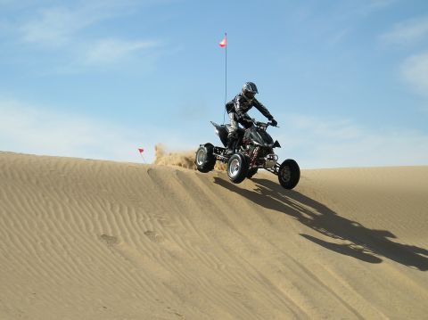 1993 Ford Bronco - Rider on a quad bike takes flight over a sand dune under a clear blue sky.