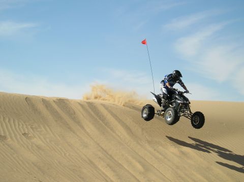 1993 Ford Bronco - A quad bike soars through the air while cresting a sand dune, leaving a trail of dust behind.
