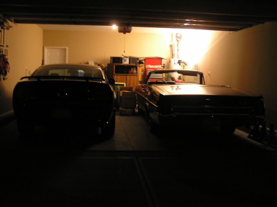 Black modern Mustang and a classic convertible in a dark garage