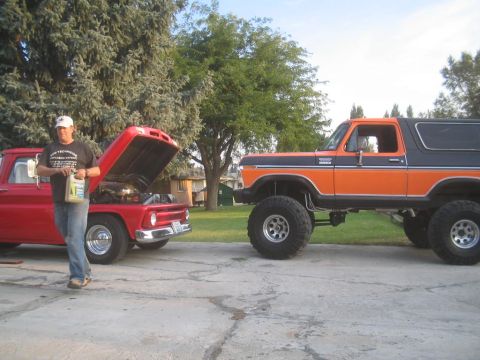 1979 Ford Bronco - A lifted 1979 Ford Bronco in orange and black is parked next to a red pickup truck with its hood open.