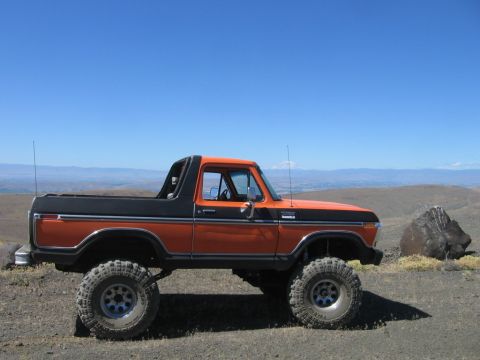 1979 Ford Bronco - This lifted Ford Bronco is parked on a rocky, elevated terrain under a clear blue sky.