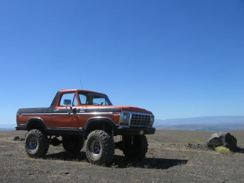 1979 Ford Bronco - A lifted 1978 Ford Bronco with an orange body and black top sits on a rocky incline.
