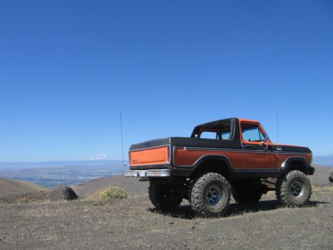 1979 Ford Bronco - A lifted 1979 Ford Bronco in orange and black sits on a rocky hill under a clear blue sky.