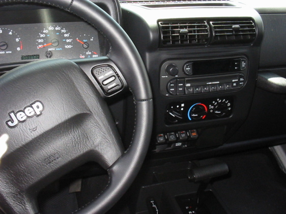 Jeep TJ interior showing steering wheel with cruise control buttons, dashboard gauges, and center console with radio and climate controls