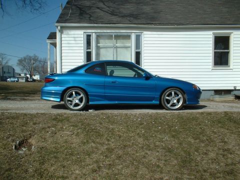 2000 Ford Escort - Side view of a blue 2000 Ford Escort coupe parked in front of a house.