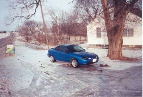 2000 Ford Escort - A blue 2000 Ford Escort coupe sits parked on a snowy drive next to a house.