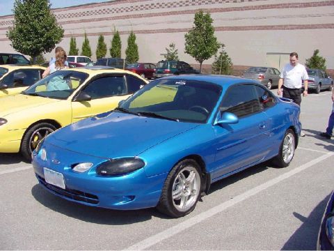 2000 Ford Escort - A blue coupe is parked in a lot next to a yellow car and other vehicles.