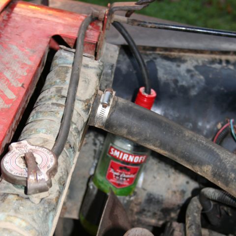 1979 Jeep CJ5 - A Smirnoff bottle is repurposed as a coolant reservoir in this vehicle's engine bay.