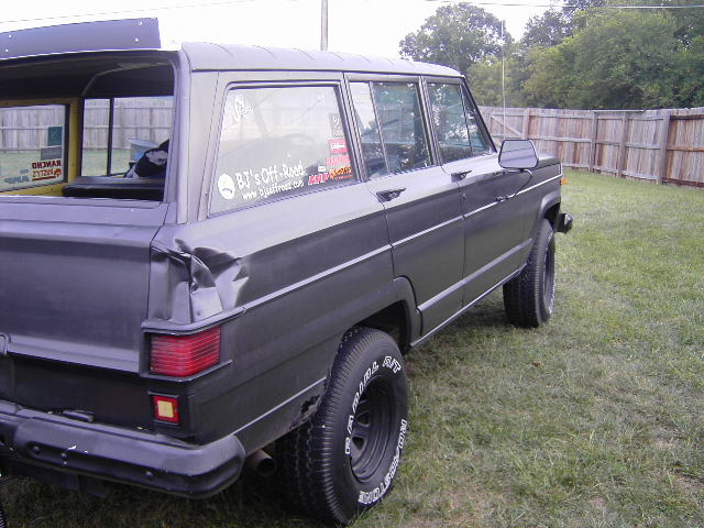 Dark gray Jeep Grand Wagoneer parked on grass, rear quarter panel is dented