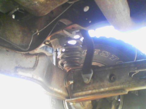 1984 Ford Bronco - Underbody shot of a rear coil spring and axle housing with a black webbing limit strap running from a bracket on the axle up to a frame mou…
